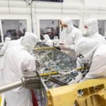 Engineers and technicians inside a clean room connecting sections of electrical wiring harness to components inside NASA's Dragonfly rotorcraft lander