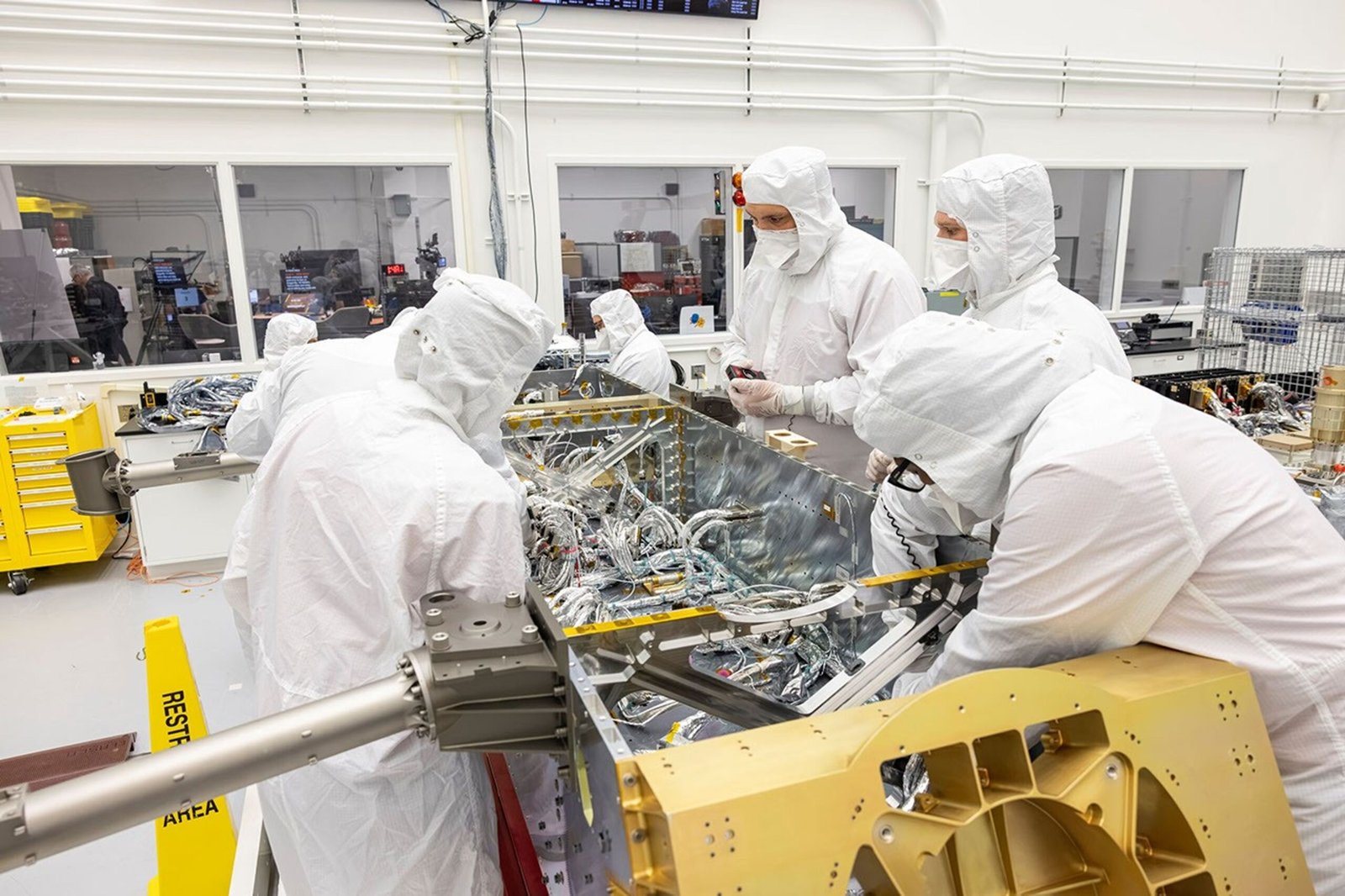 Engineers and technicians inside a clean room connecting sections of electrical wiring harness to components inside NASA's Dragonfly rotorcraft lander